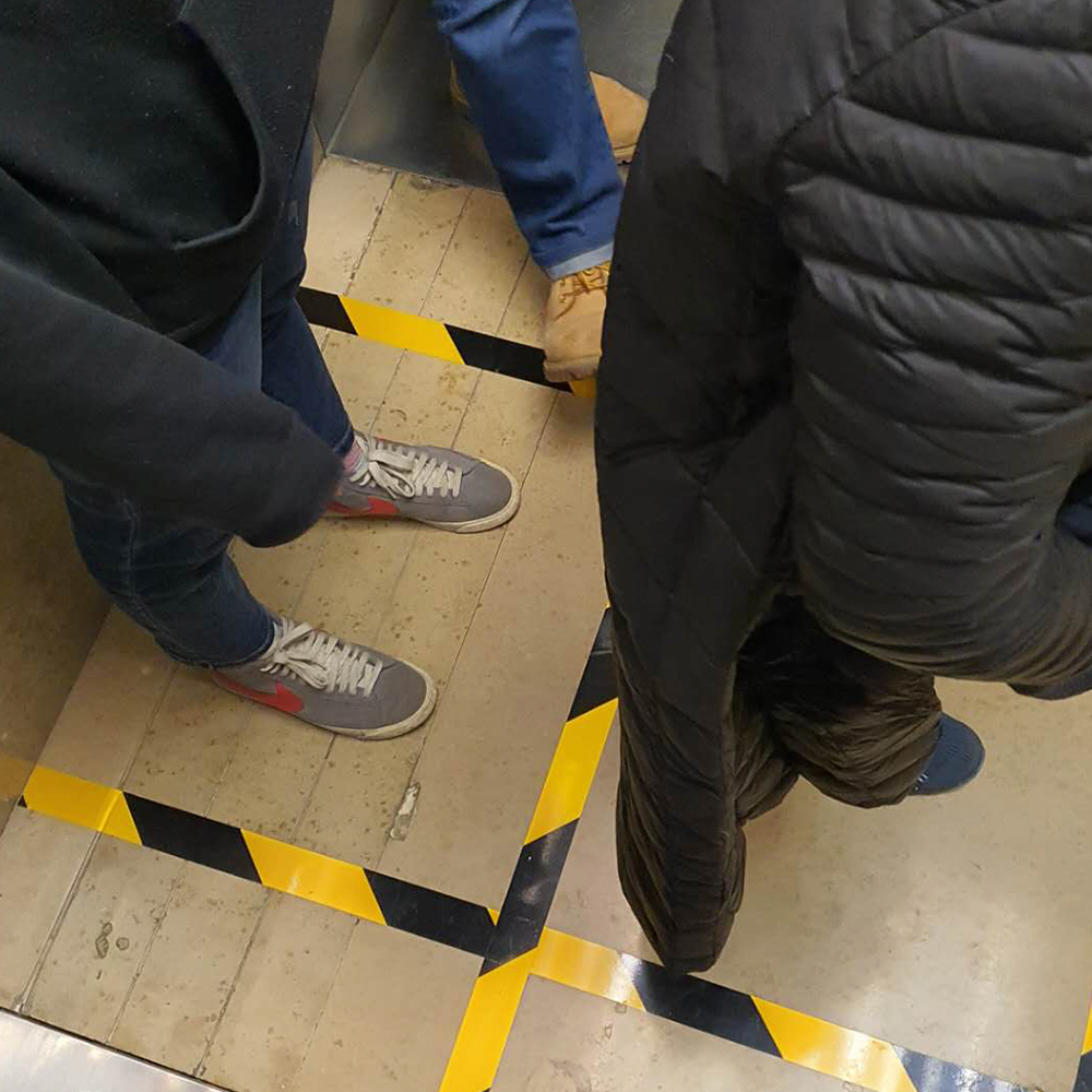 Occupants of an elevator standing inside a grid marked with black and yellow 'caution' tape