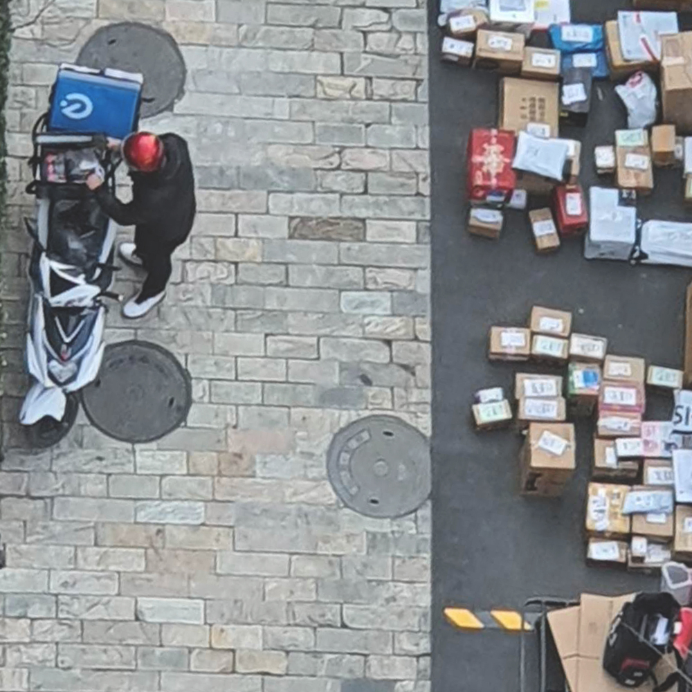 kuadi driver on a scooter unloading parcels to a residential dropoff zone